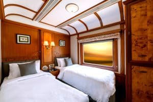Cabine twin du Deccan Odyssey avec boiseries luxueuses, lits jumeaux et fen&ecirc;tre panoramique au coucher du soleil